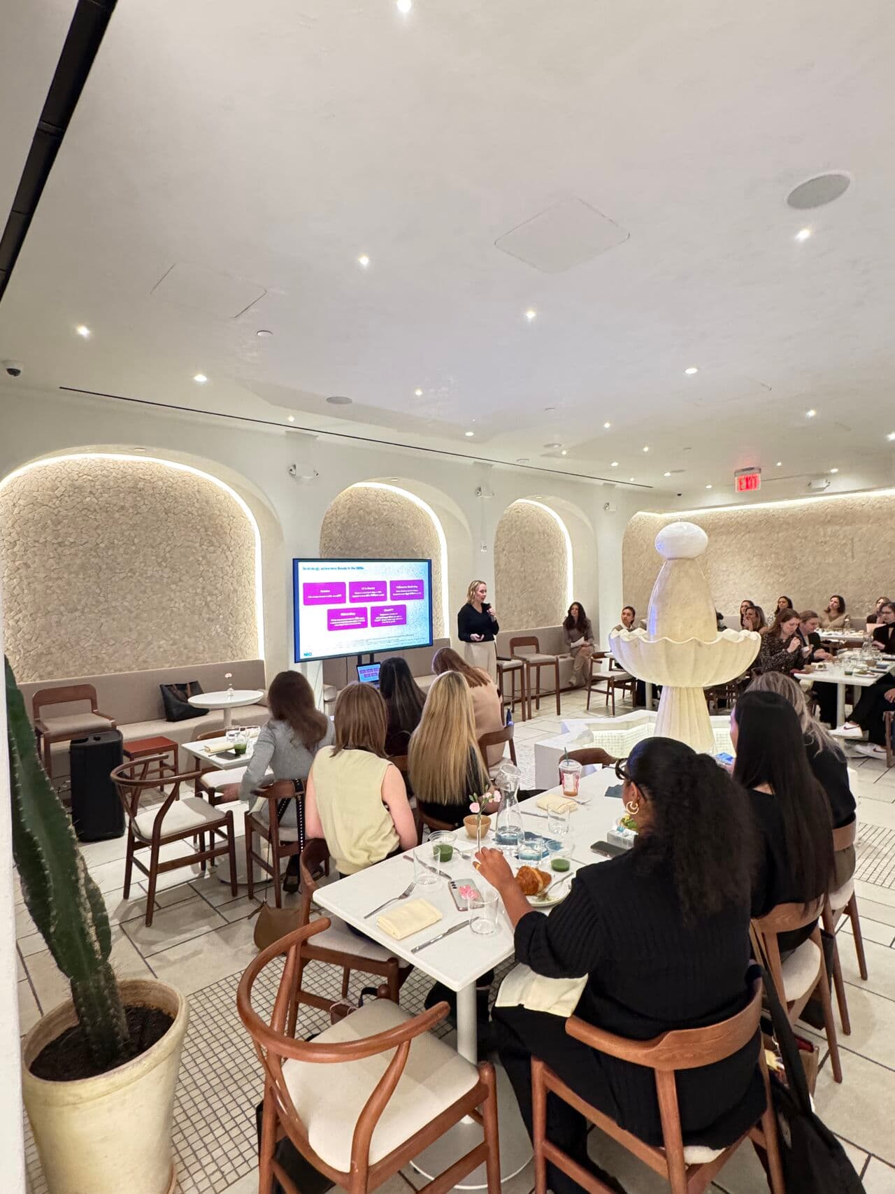 Attendees at Revieve's AI Beauty Breakfast in New York City watching a presenter speak in front of a slide